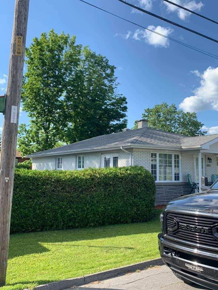 Une maison basse et claire, avec une haie verte devant, par une journée ensoleillée.