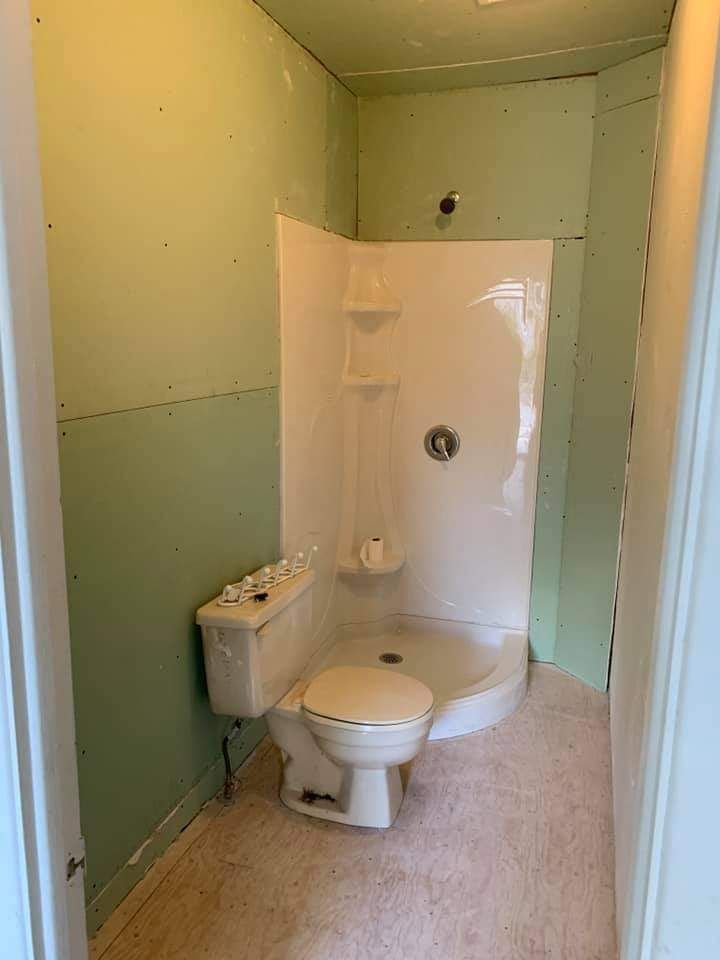 Rénovation de salle de bain : murs verts, cabine de douche blanche, toilettes et sol beige.