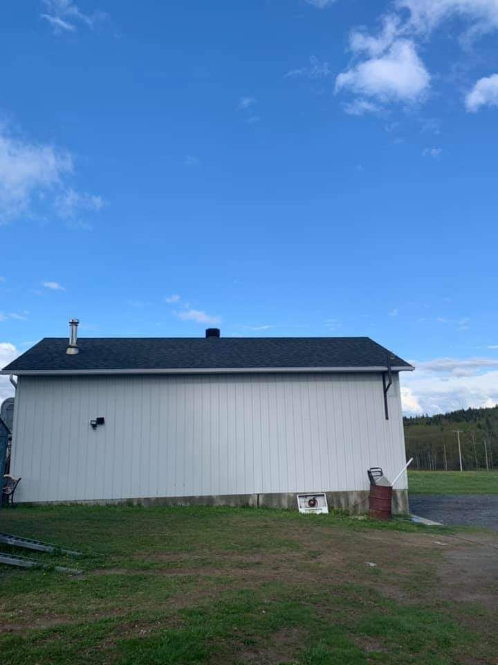 Bâtiment blanc au toit noir se détachant sur un ciel bleu, au milieu d'un champ herbeux.