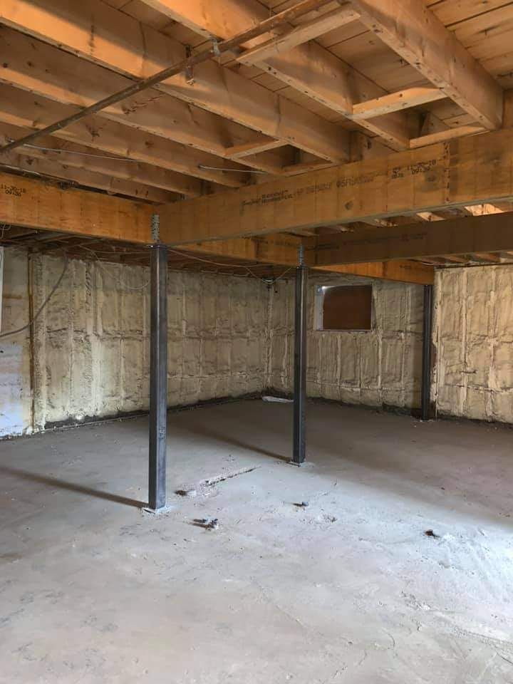 Intérieur du sous-sol avec poutres apparentes, sol en béton, poteaux de soutien et murs isolés.