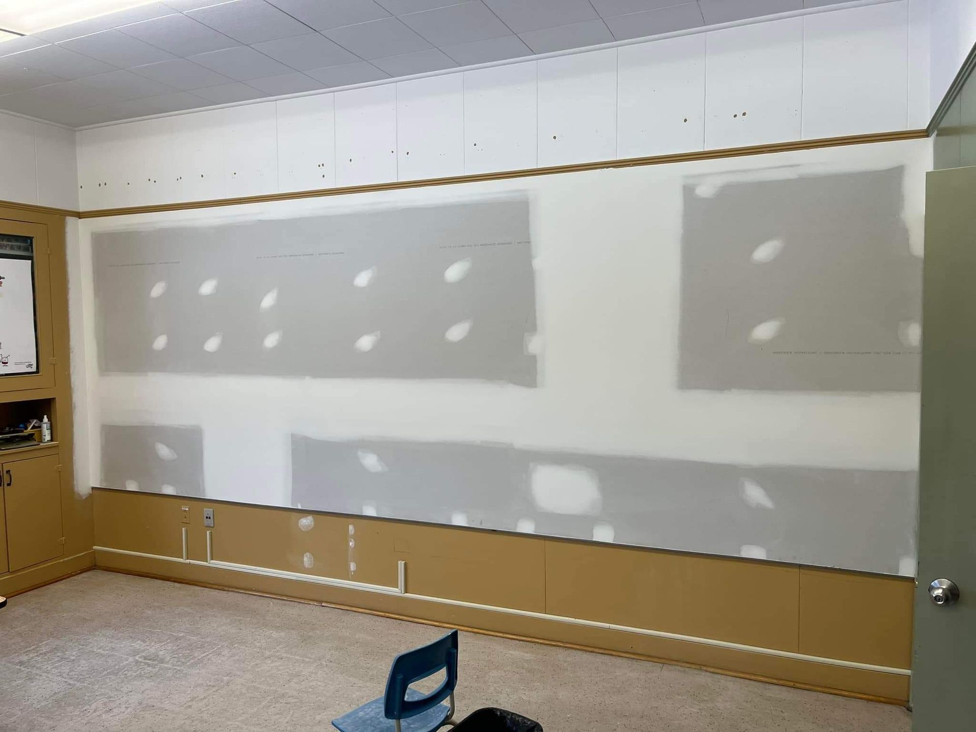 Pièce avec des plaques de plâtre réparées sur un mur blanc, des moulures en bois et des armoires.