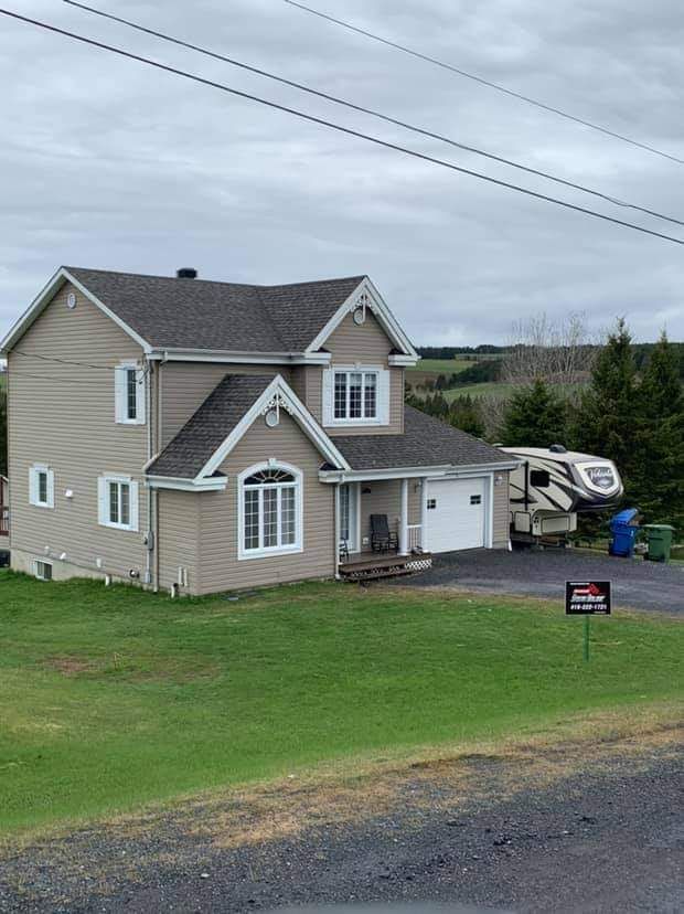 Maison beige à deux étages avec boiseries blanches, garage attenant et camping-car garé dans l'allée sur une pelouse verte.