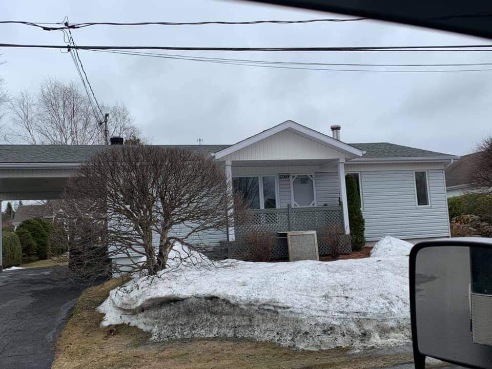 Petite maison de plain-pied avec porche et abri voiture ; neige au sol. Ciel couvert.
