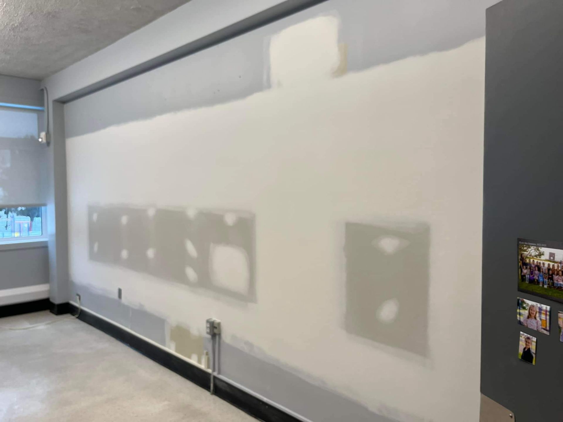 Mur intérieur avec des réparations en plaques de plâtre, apprêté en blanc, avec des moulures et un sol gris.