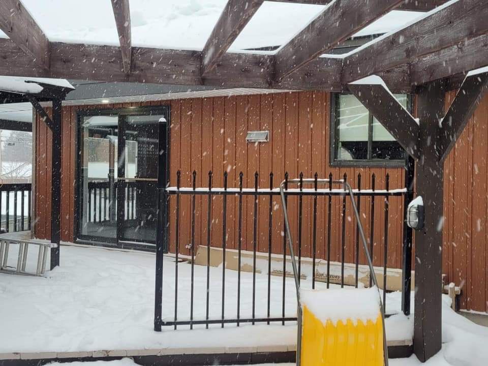Extérieur d'un bâtiment avec une terrasse enneigée, une clôture noire et une pelle à neige jaune.