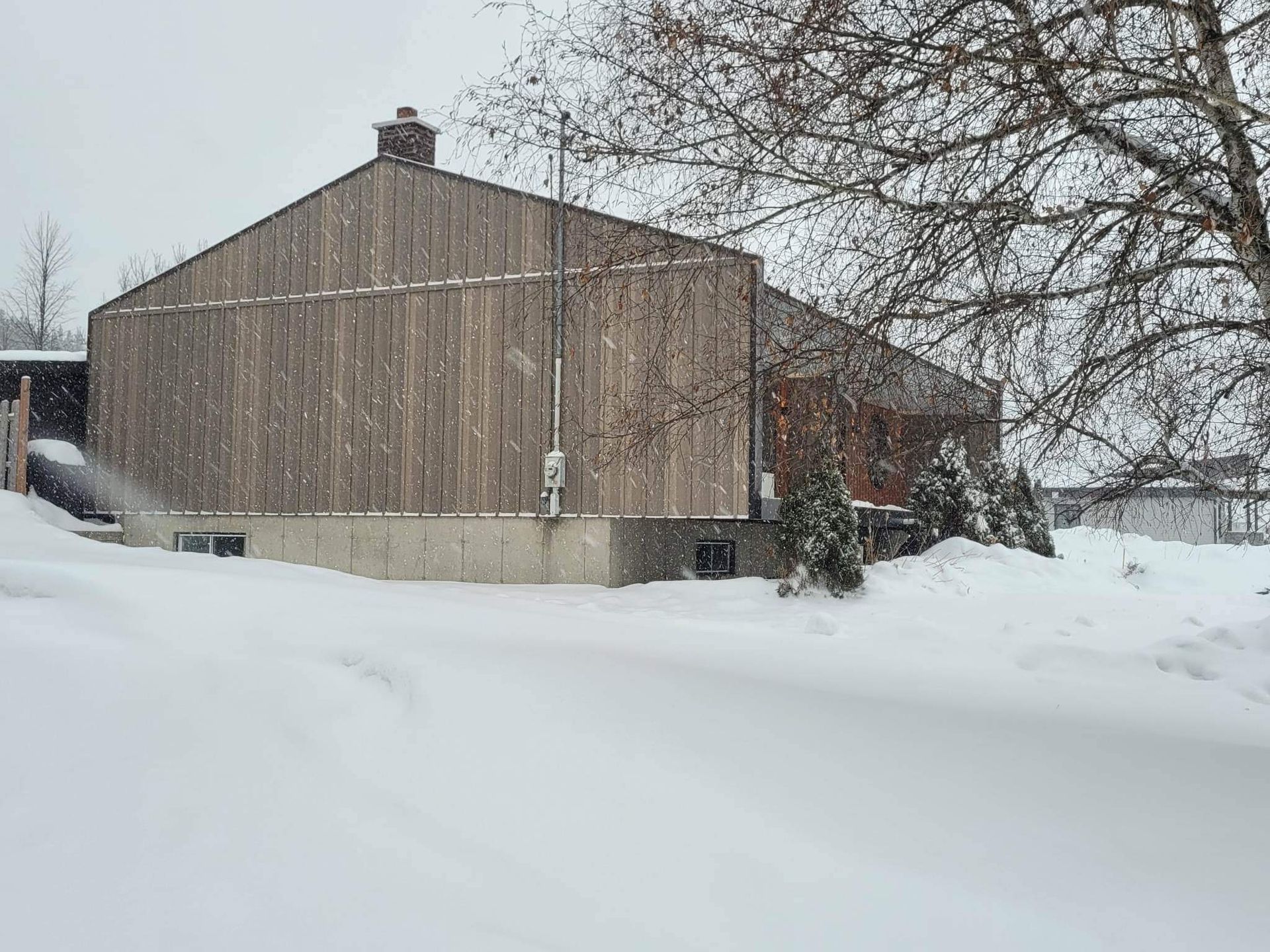 Un bâtiment en bois enneigé avec une cheminée. La scène semble se dérouler par une journée d'hiver enneigée.