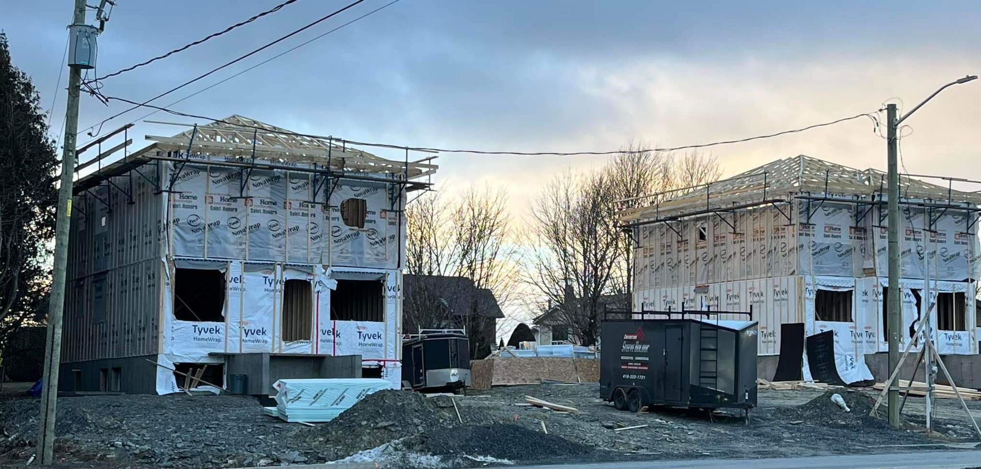 Deux maisons en construction, avec leurs charpentes et bardages en bois apparents, par temps nuageux.