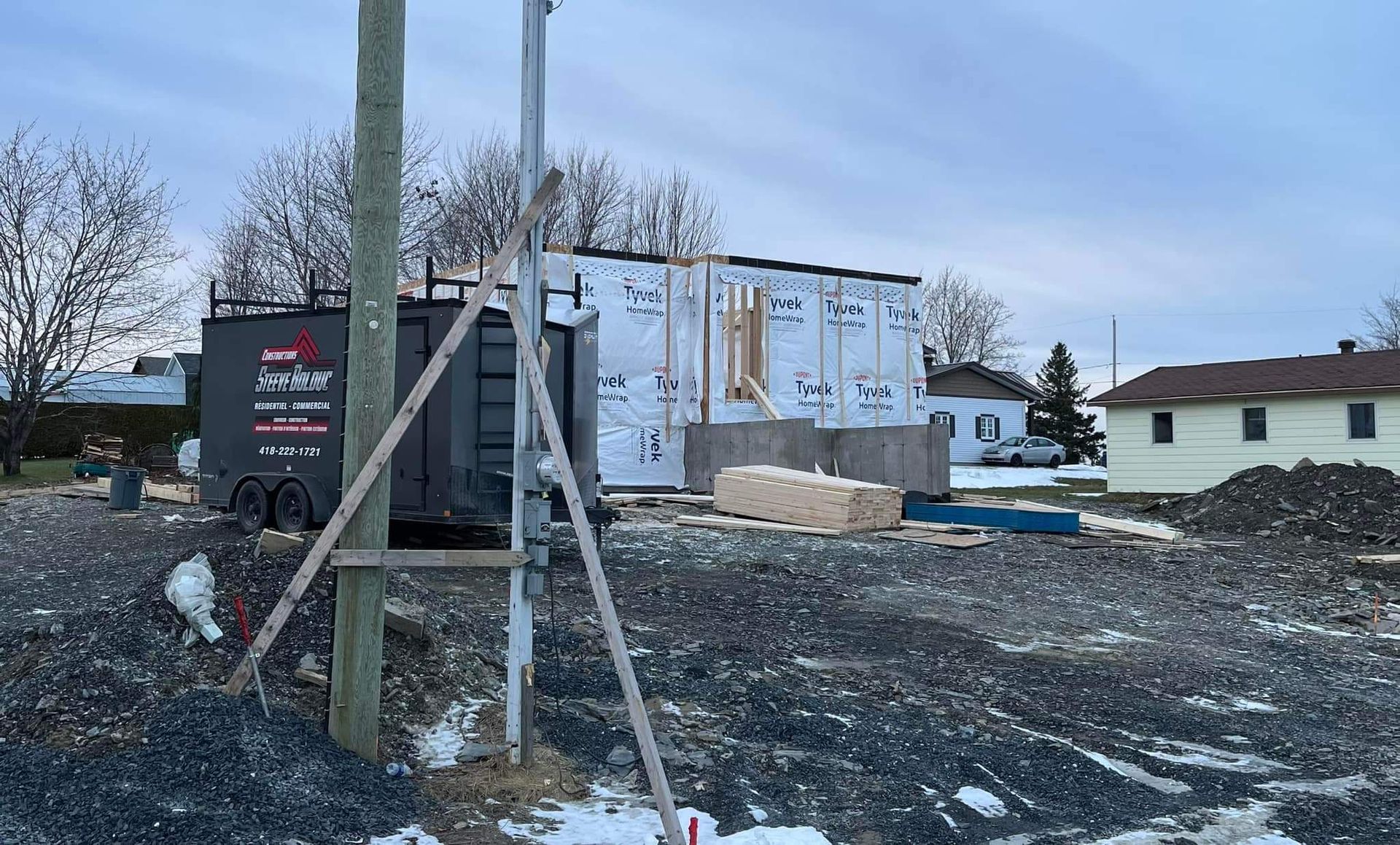 Chantier de construction avec une structure partiellement construite, une remorque et du gravier.