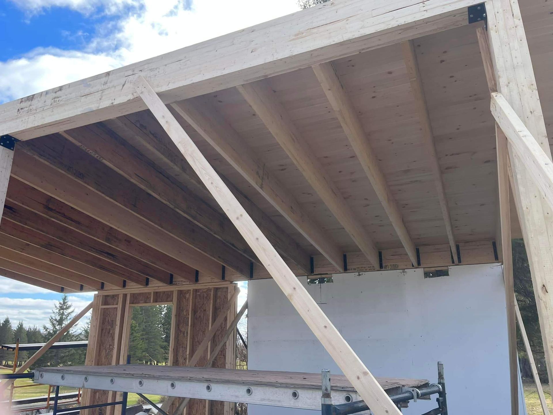 Structure en bois en construction, chevrons et poutres visibles. Un échafaudage soutient la charpente.