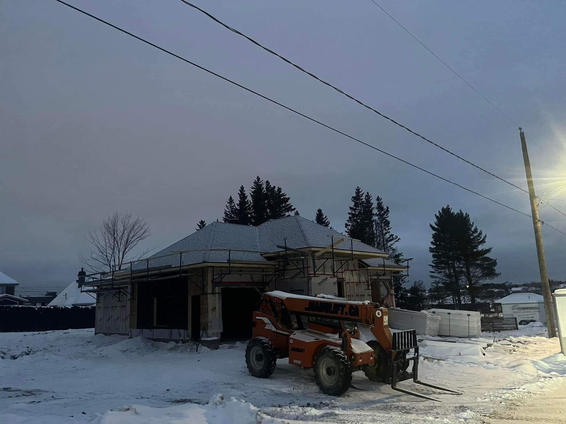 Chantier de construction avec une maison en construction, de la neige et un chariot élévateur orange.