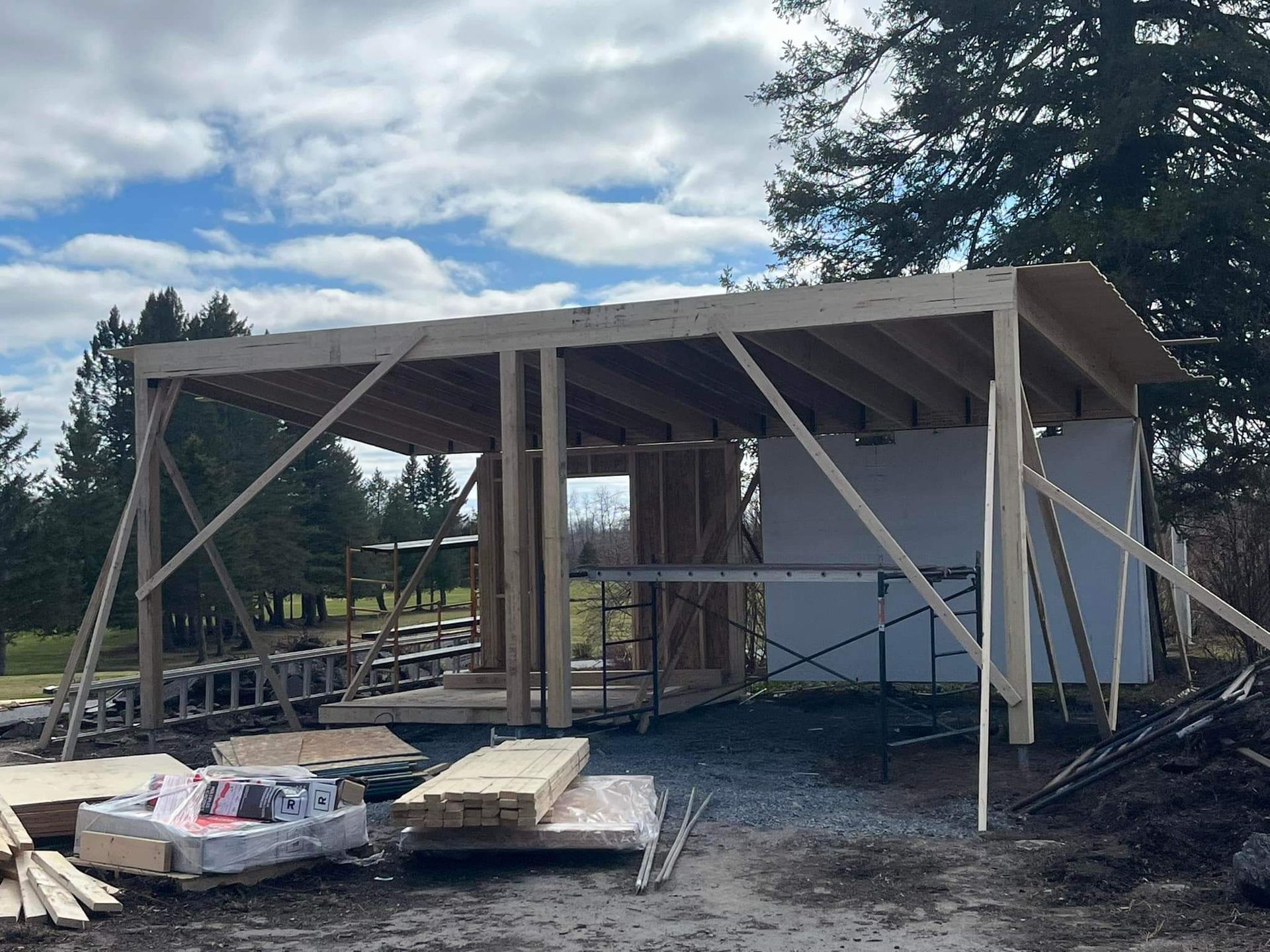 Chantier de construction d'une structure en bois, en extérieur. Ciel bleu, outils et matériaux sont visibles.