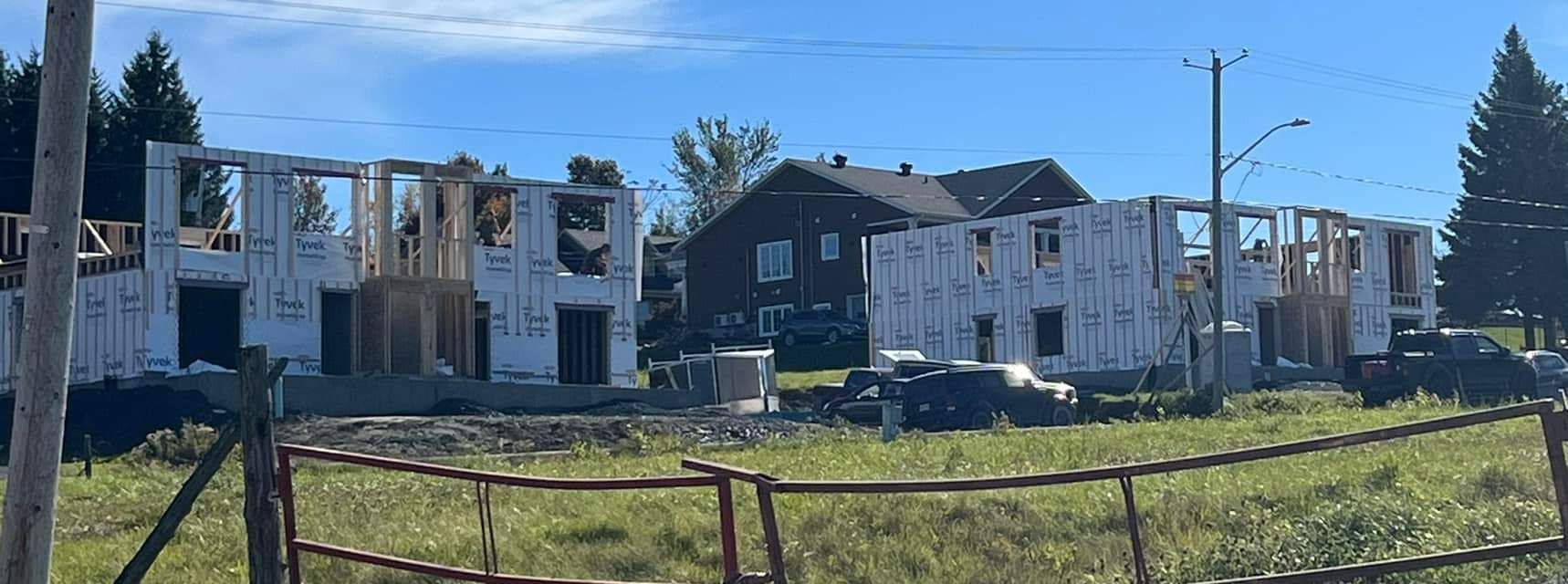 Maisons en construction ; ossature bois avec bardage blanc ; espace vert et ciel bleu.