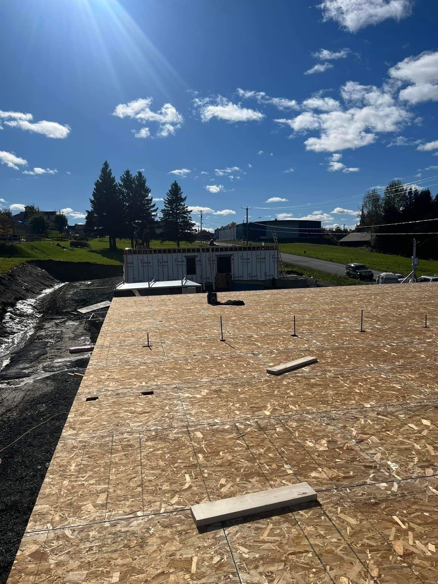 Chantier de construction avec une structure partiellement édifiée, journée ensoleillée avec un ciel bleu et quelques nuages épars.