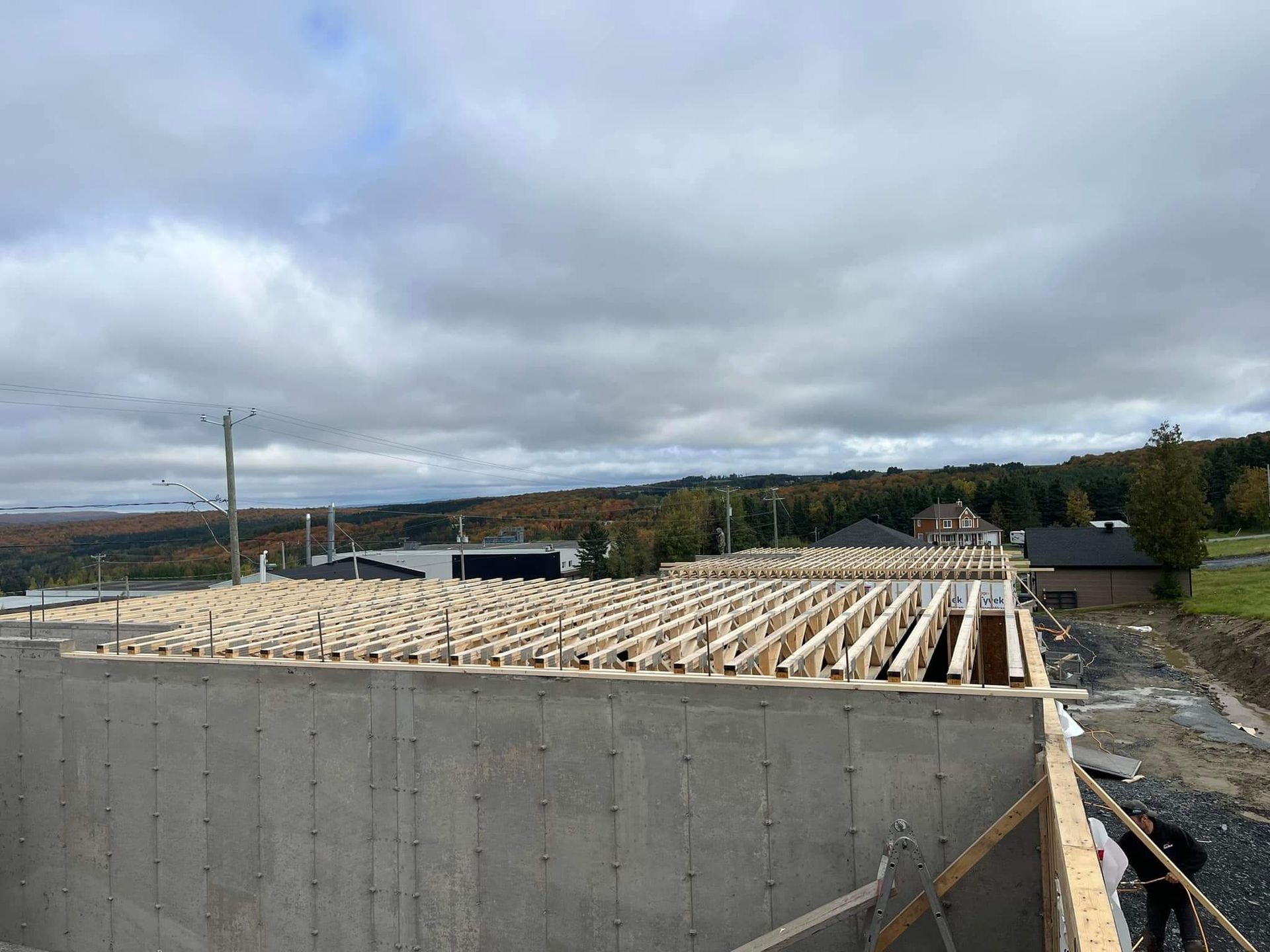 Fondations en béton avec solives en bois apparentes, sous un ciel nuageux. Chantier de construction.