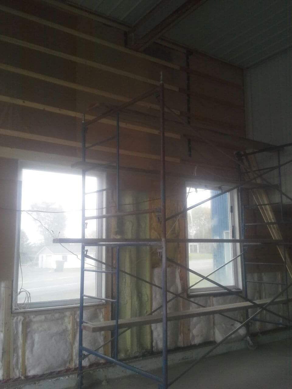 Échafaudages à l'intérieur d'un bâtiment à deux fenêtres. Les murs sont recouverts de lambris.