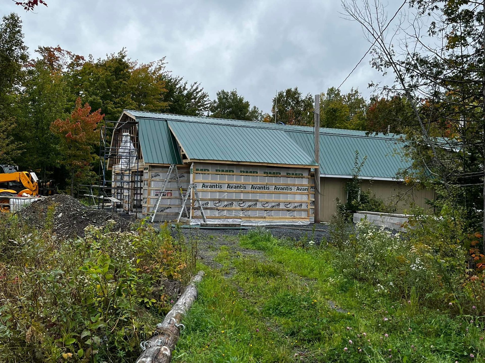Bâtiment en construction avec un toit en métal vert entouré d'arbres.