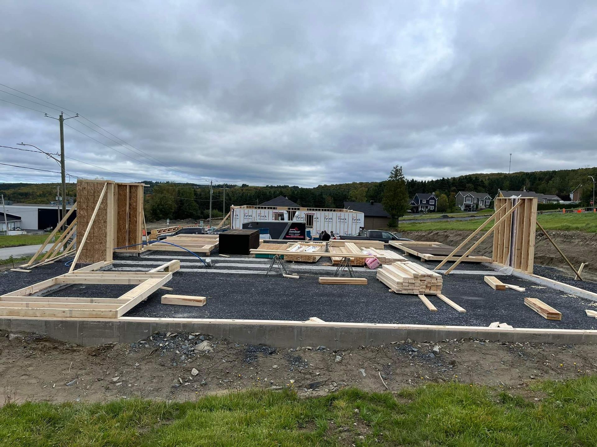 Chantier de construction avec charpente et fondations en bois, sous un ciel nuageux.
