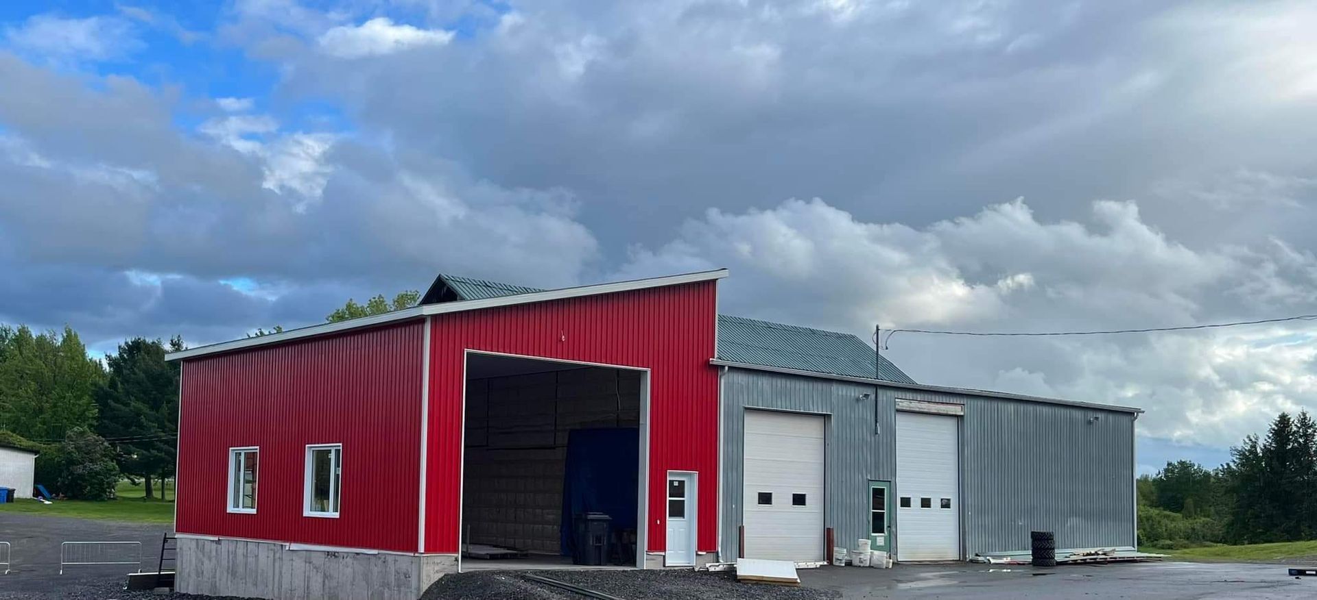 Bâtiment métallique rouge et gris avec portes coulissantes ouvertes sous un ciel nuageux.