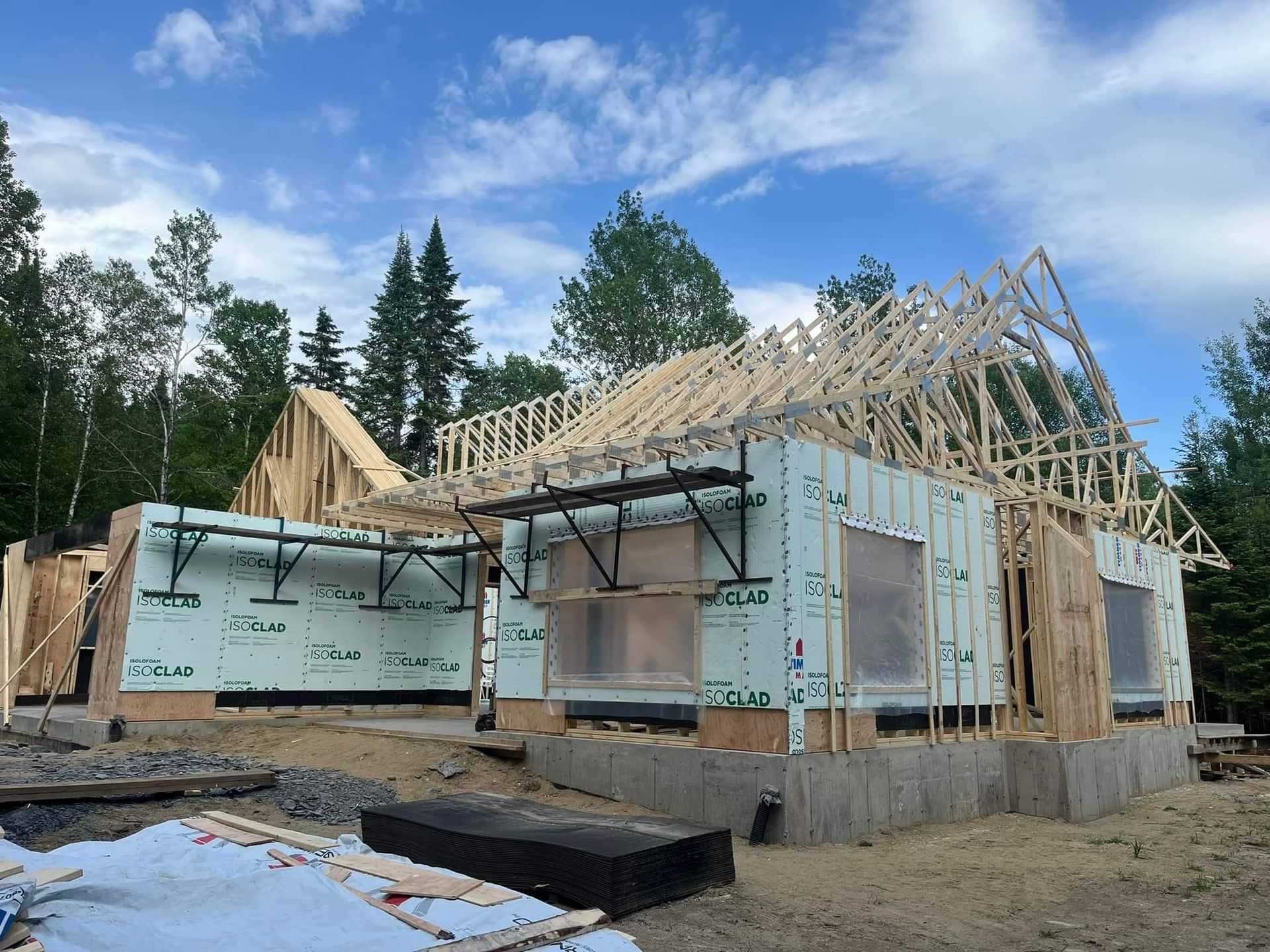 Maison en construction ; charpente en bois et isolation visibles, ciel bleu en arrière-plan.