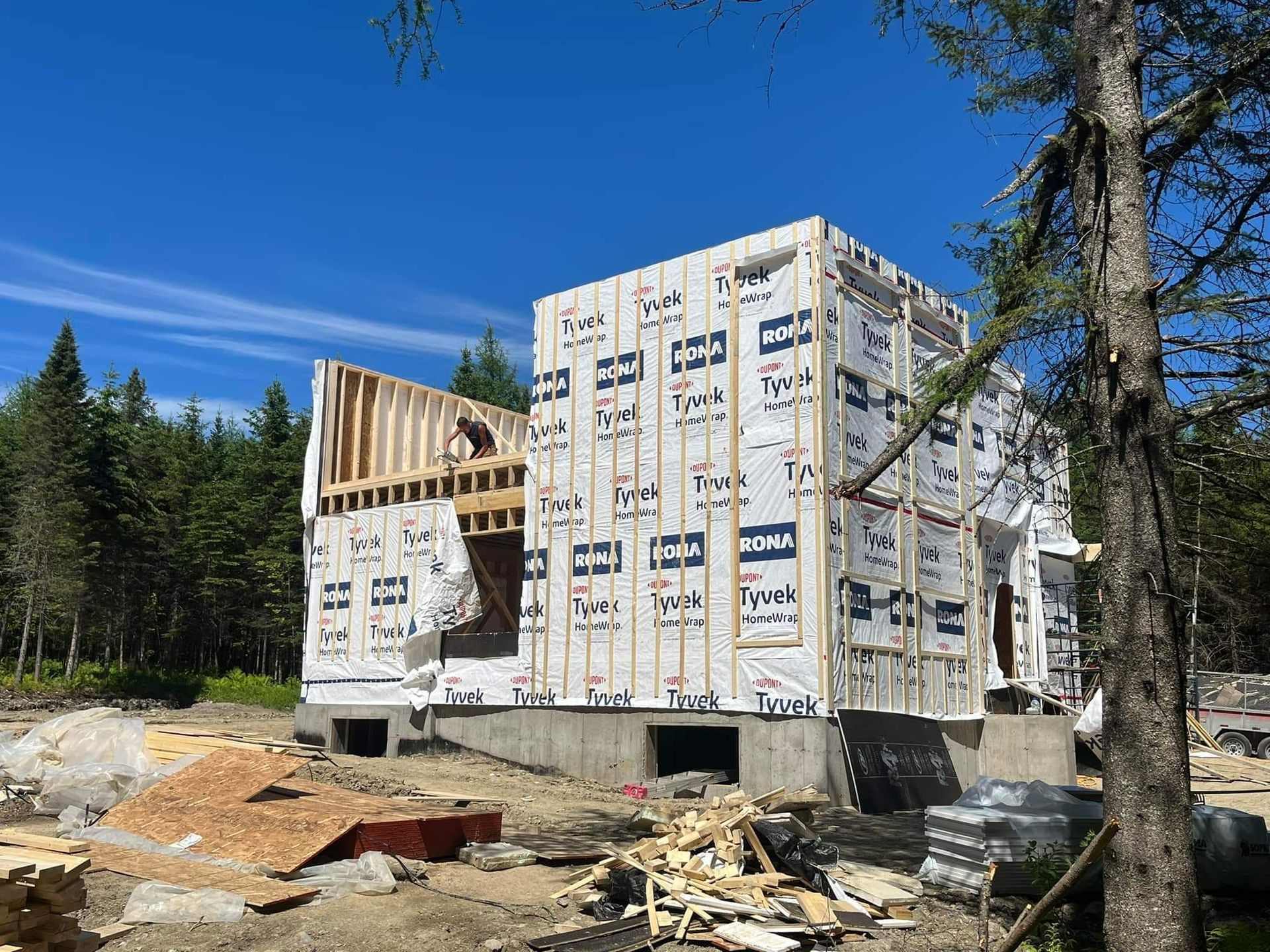 Construction d'un bâtiment à ossature bois, recouvert d'un revêtement résistant aux intempéries, sur des fondations en béton, sous un ciel bleu.
