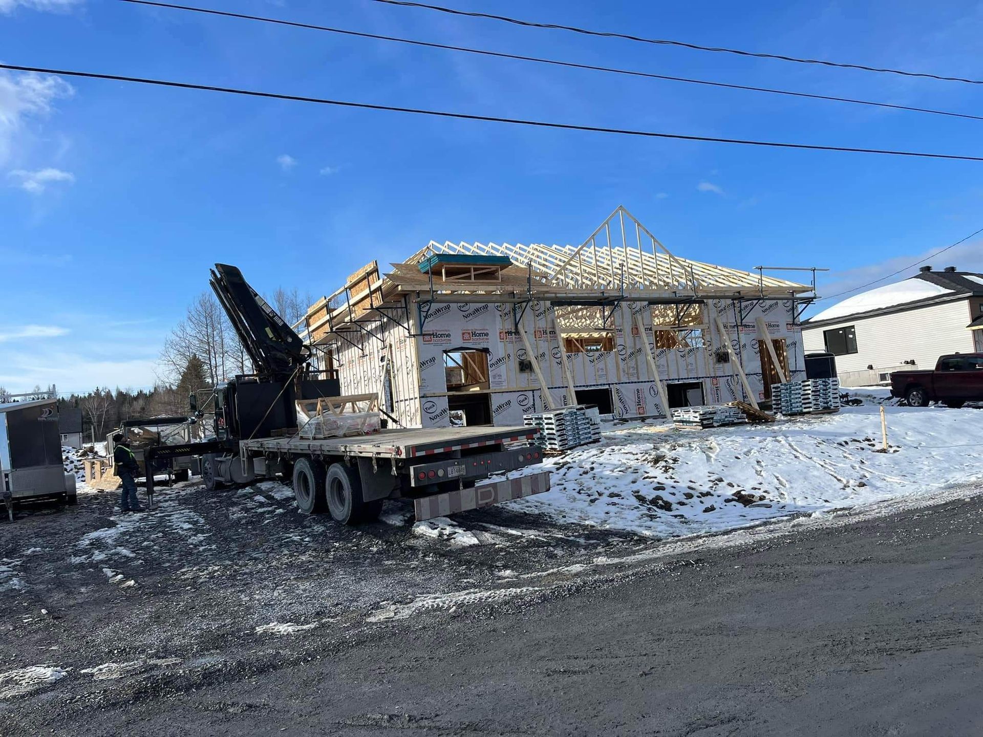 Chantier de construction : Un camion-grue près d'une structure de bâtiment recouverte d'isolant par une journée enneigée.