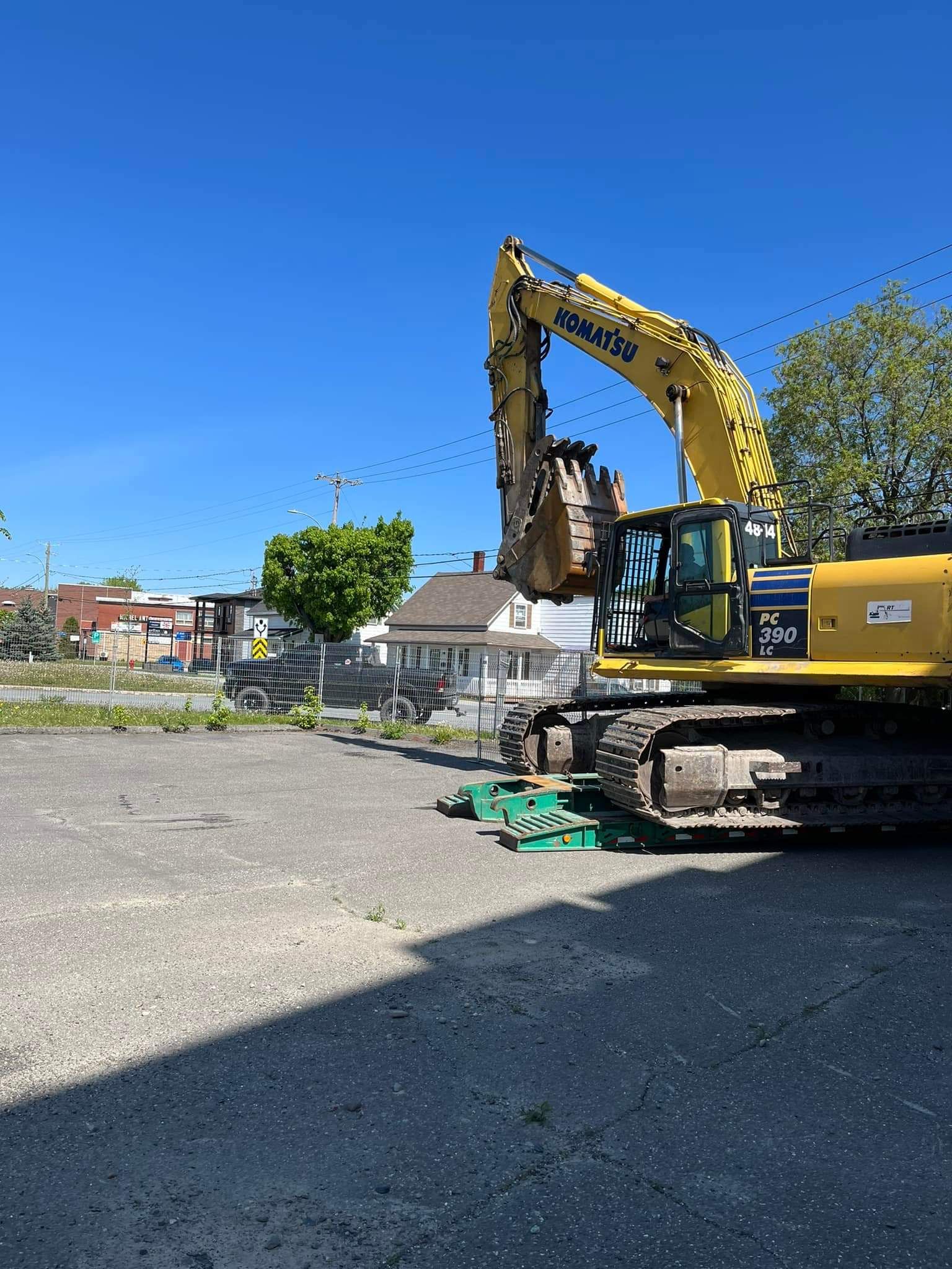 Une pelleteuse Komatsu jaune démolit un bâtiment sous un ciel bleu azur.