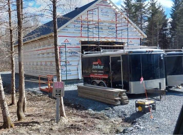 Chantier : bâtiment à ossature recouverte de bâche Tyvek, remorques, bois d'œuvre et générateur.