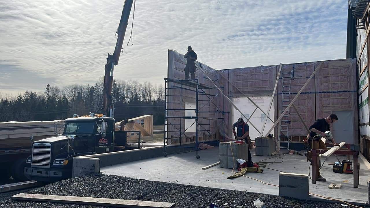 Des ouvriers du bâtiment construisent une structure, utilisant une grue pour soulever des matériaux, à l'extérieur par temps nuageux.