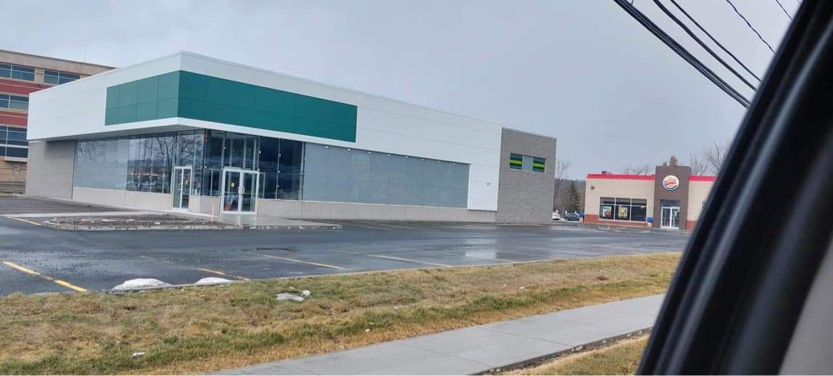 Un bâtiment gris et blanc avec une touche de vert à côté d'un Taco Bell par temps pluvieux.
