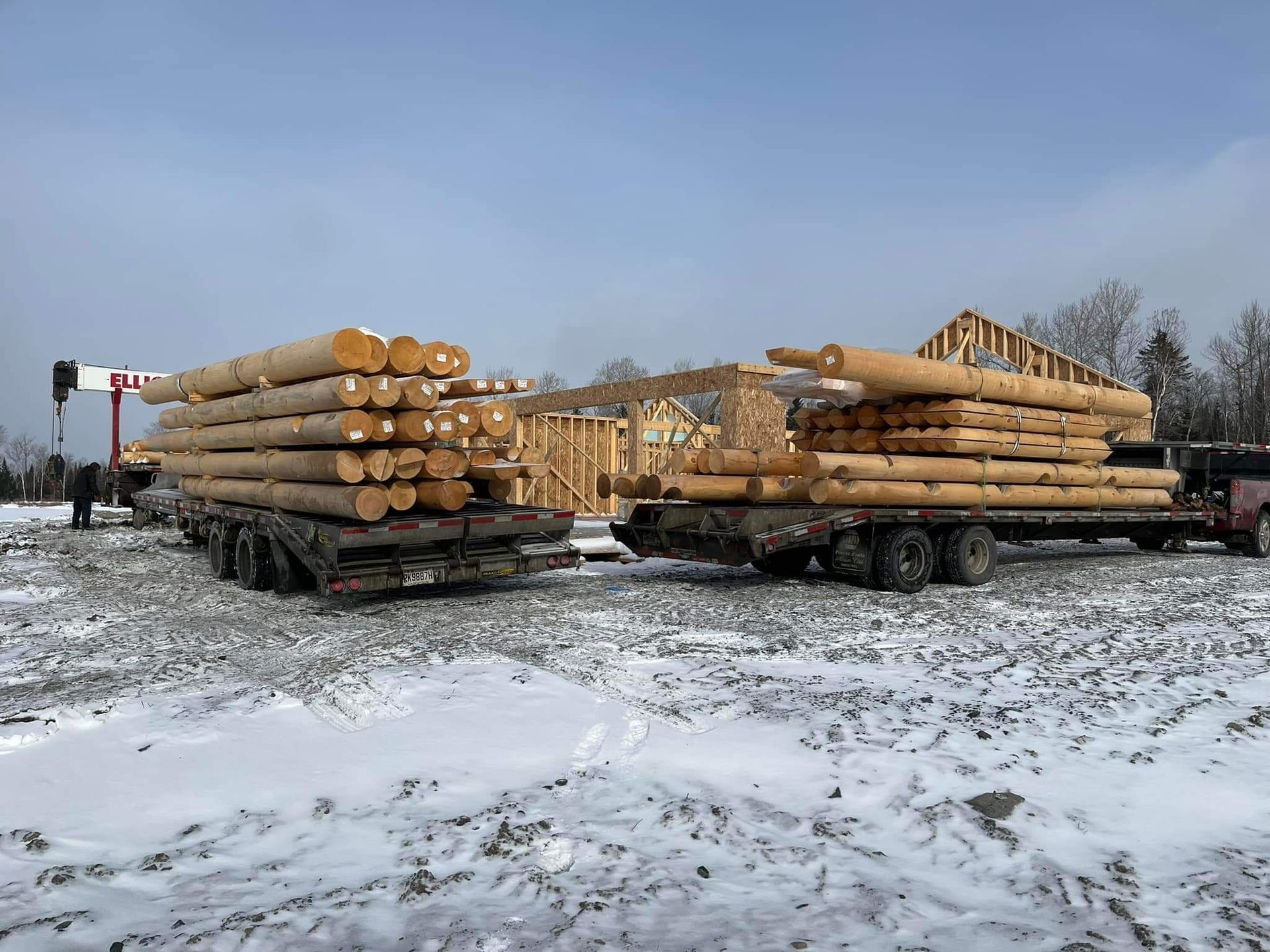 Deux camions chargés de grumes sur un chantier de construction, dans des conditions enneigées.