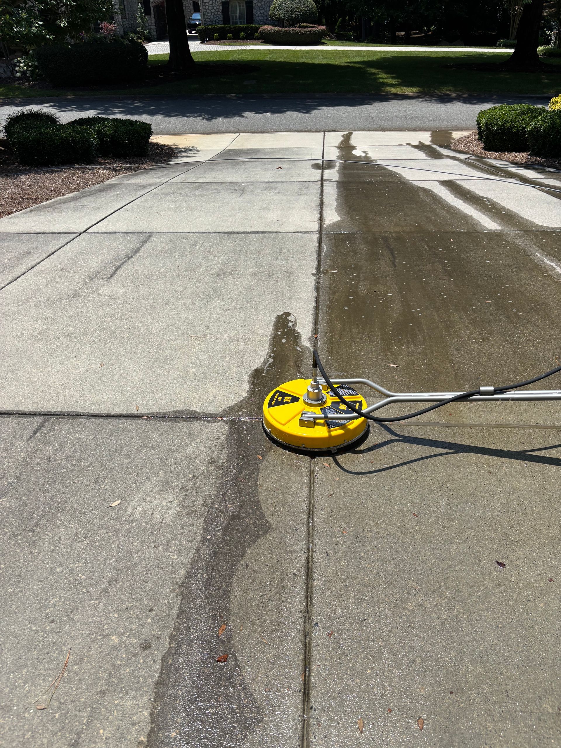 Windows Gutters LLC - Yellow circular power washer cleaning a concrete driveway outside.