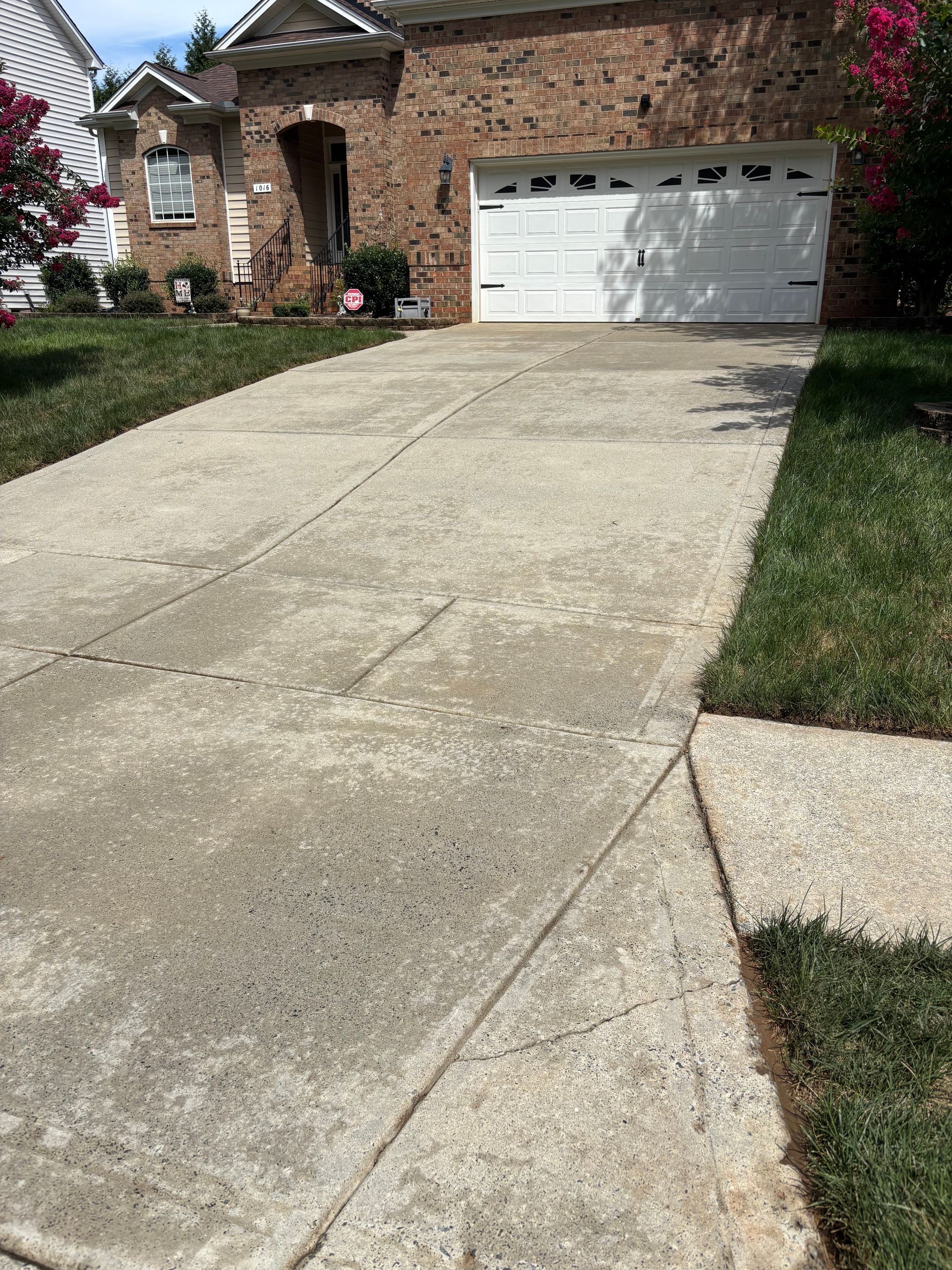 Windows Gutters LLC - Concrete driveway leading to a brick house with a white garage door. Green grass borders the driveway.