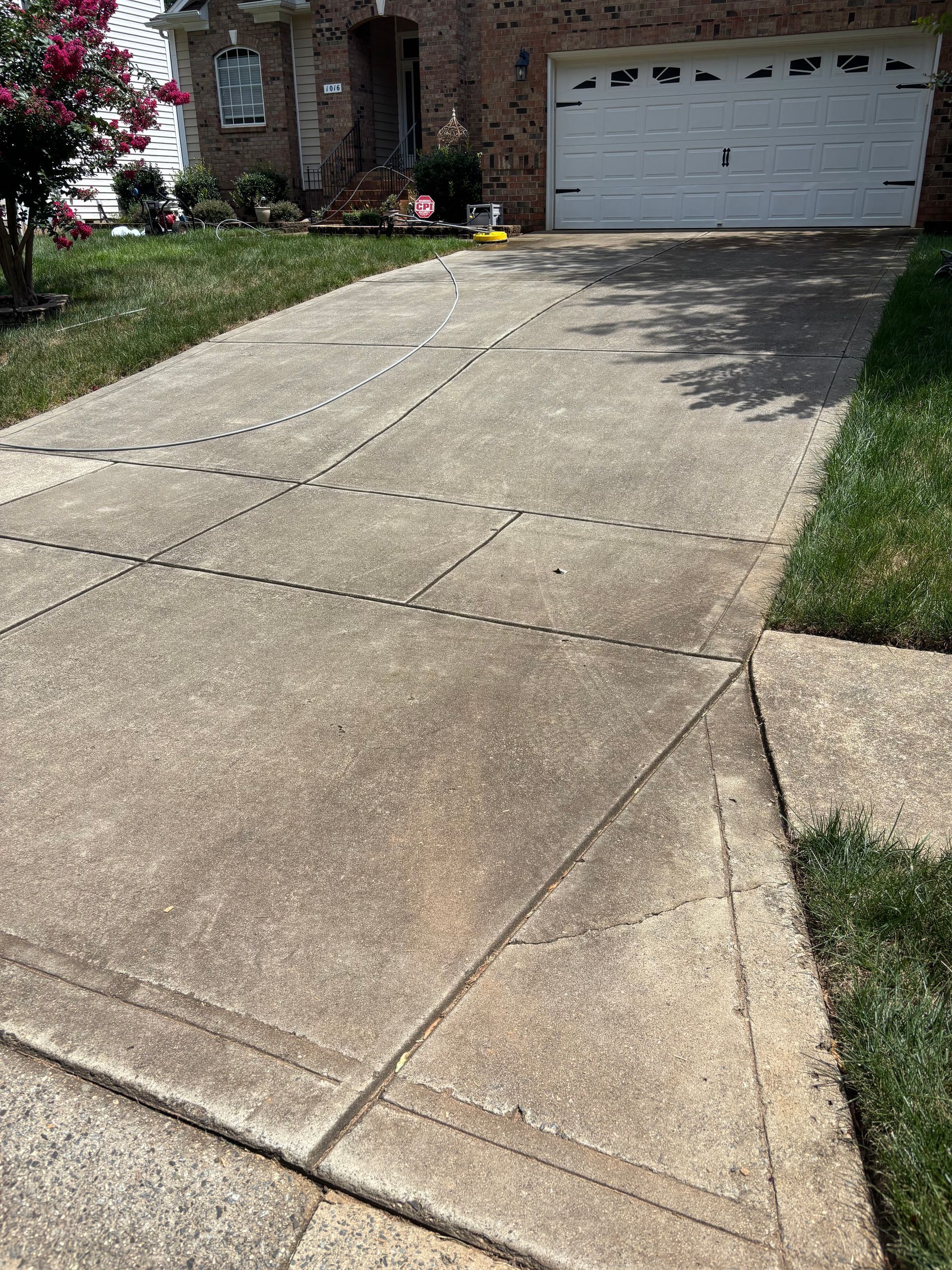 Windows Gutters LLC - Concrete driveway with cracks, leading to a garage; green grass borders the sides of the driveway.