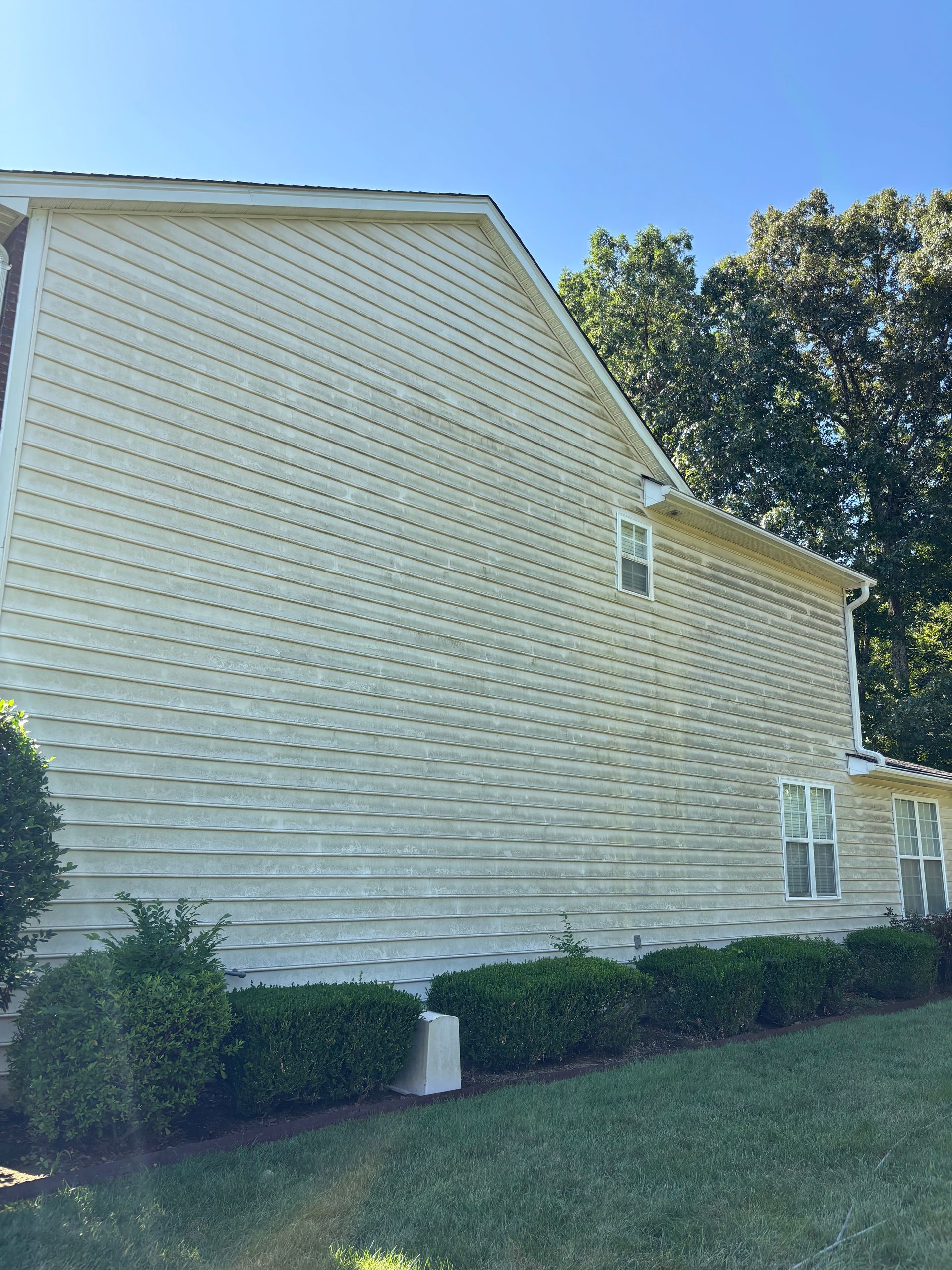 Windows Gutters LLC - Tan-sided house, green bushes, trees and lawn under a blue sky.