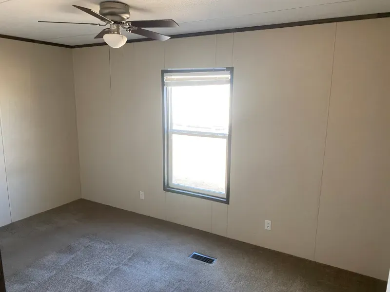 An empty bedroom with a ceiling fan and a window.