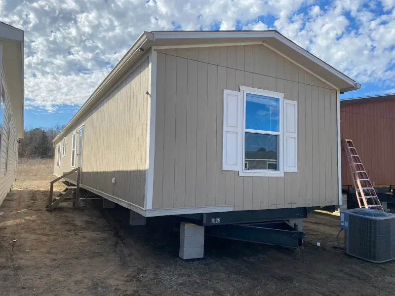 A mobile home is sitting on top of a trailer in a field.