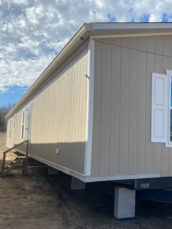 A mobile home is sitting on top of a trailer in a dirt field.