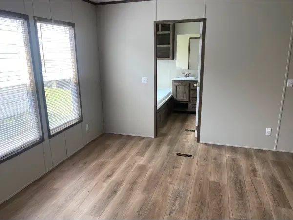An empty room with hardwood floors and a door leading to a bathroom.