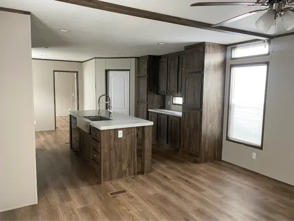 A living room with a kitchen and a ceiling fan in a mobile home.