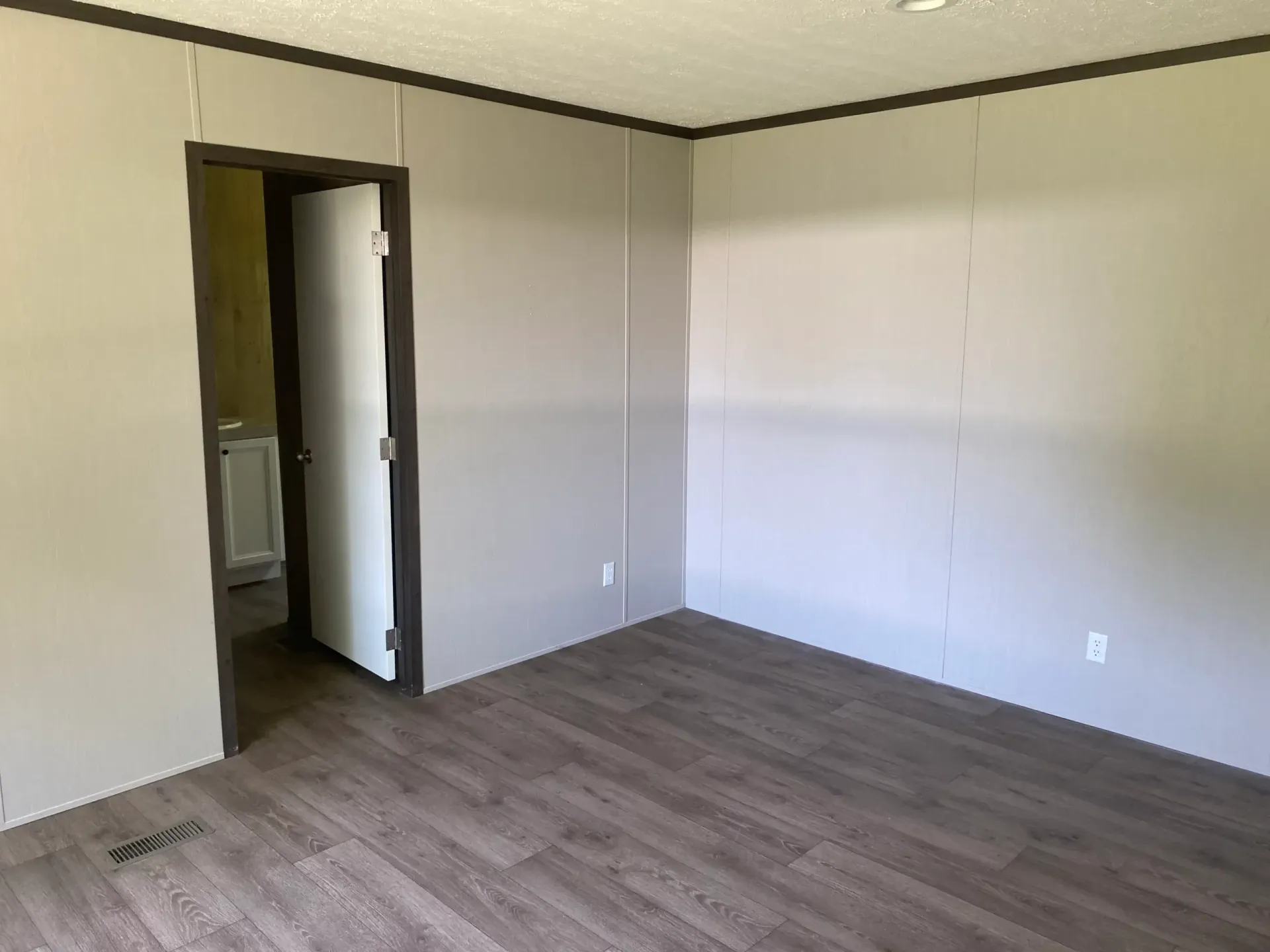An empty room with hardwood floors and a door leading to a bathroom.
