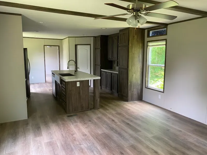 A living room with a ceiling fan and a kitchen in a mobile home.