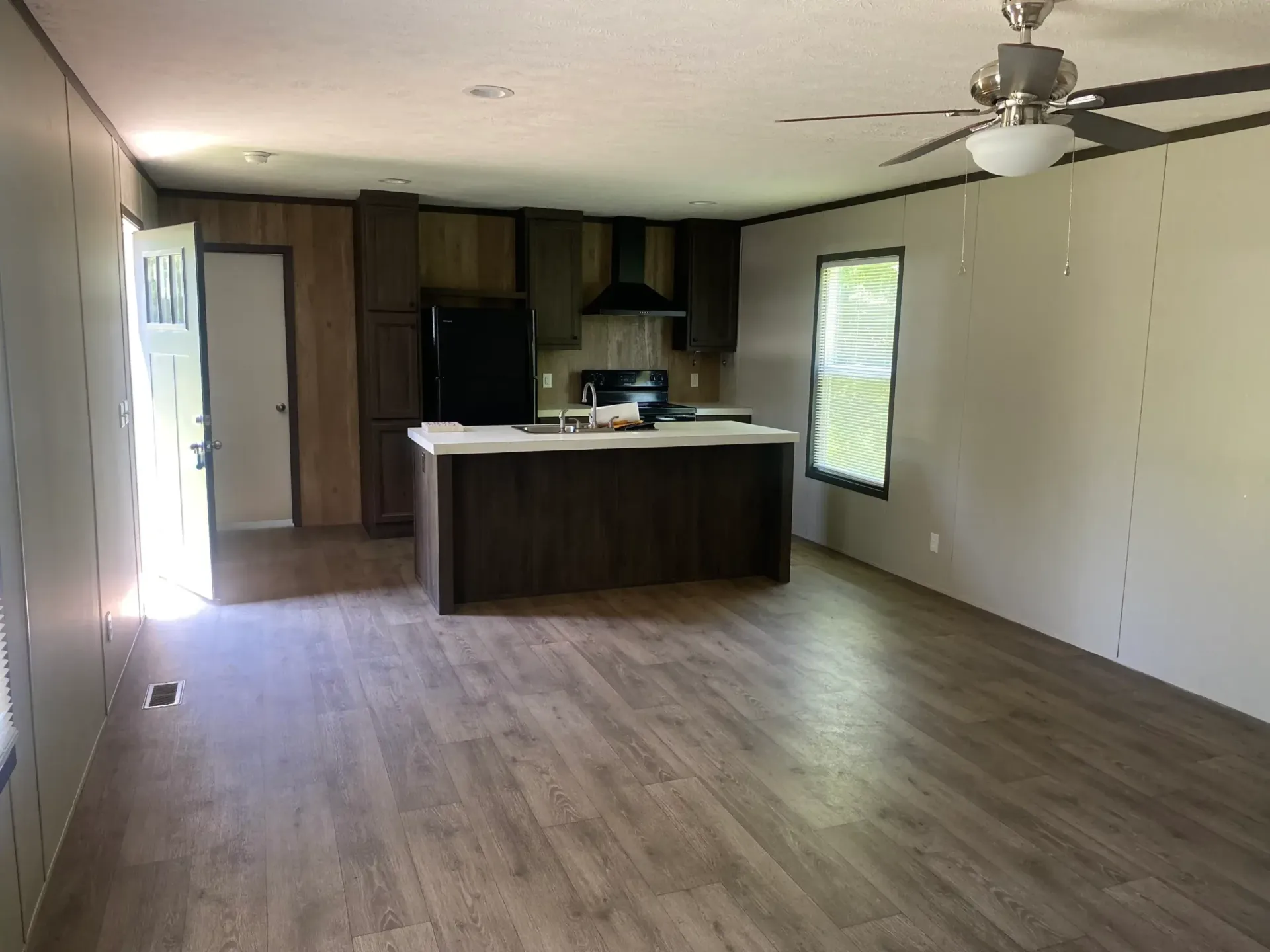 A living room with a kitchen and a ceiling fan.