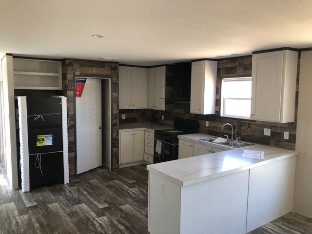 An empty kitchen with white cabinets and a black refrigerator.