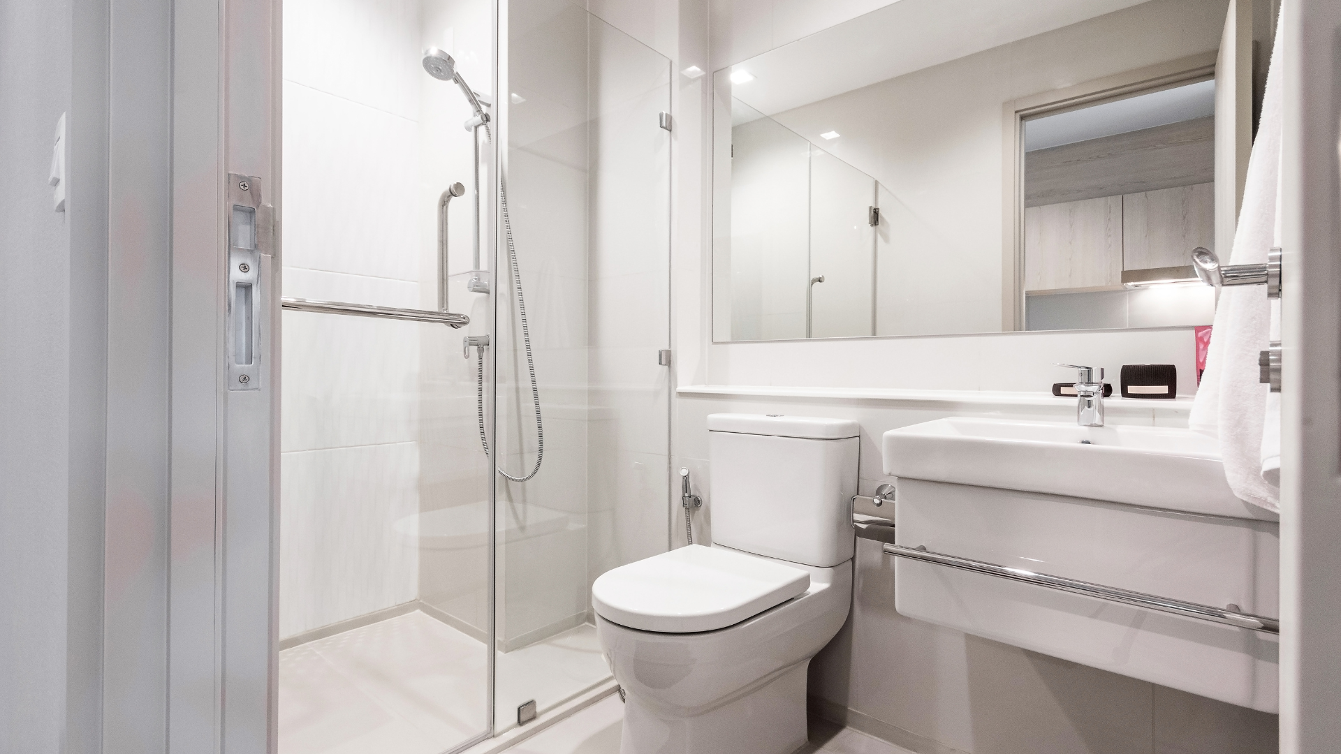 Bright, modern bathroom with a toilet, sink, and glass-enclosed shower. White walls and fixtures dominate the space.