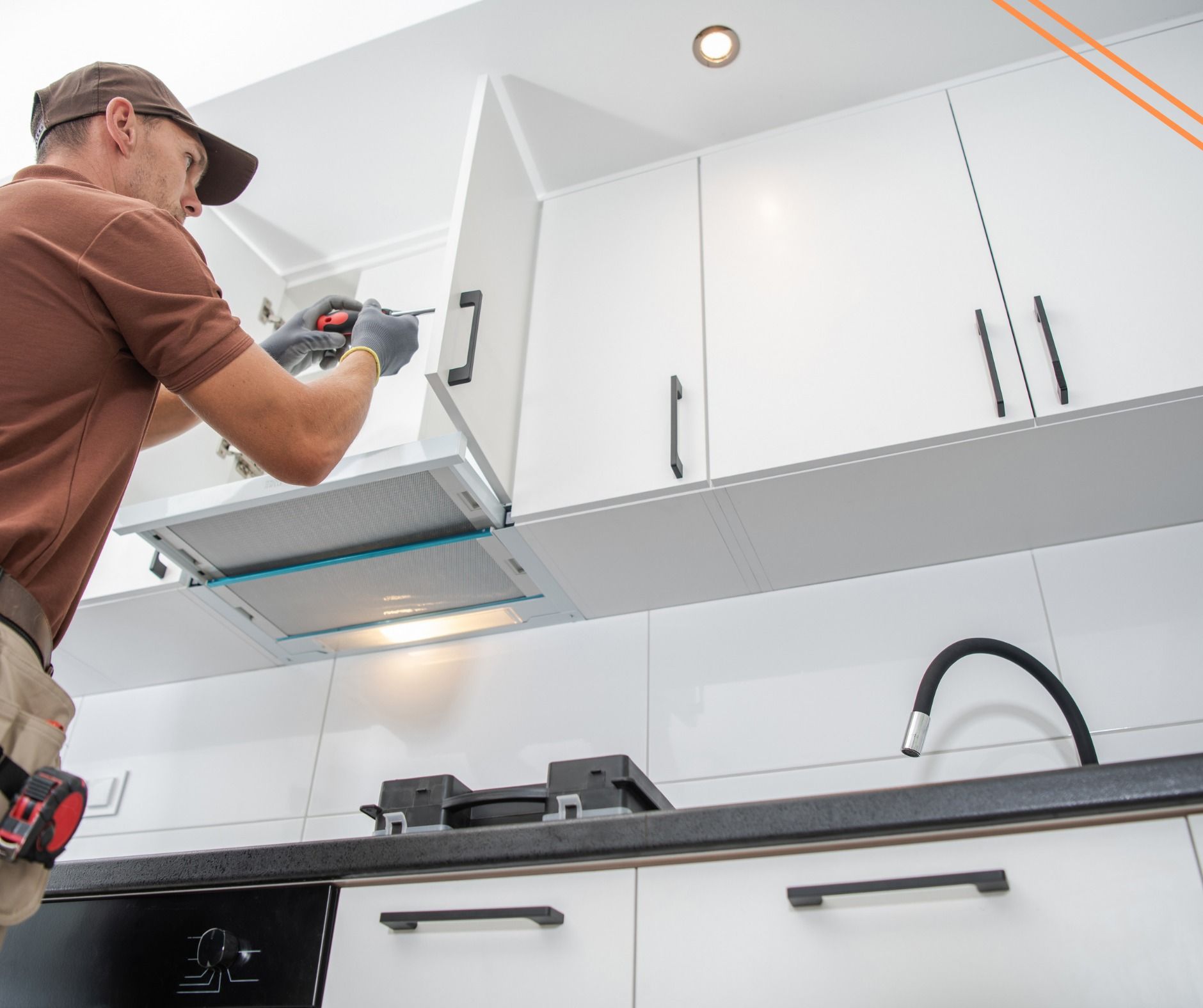 A person is installing a white kitchen cabinet above a stovetop. They are using a power tool, in a white kitchen.