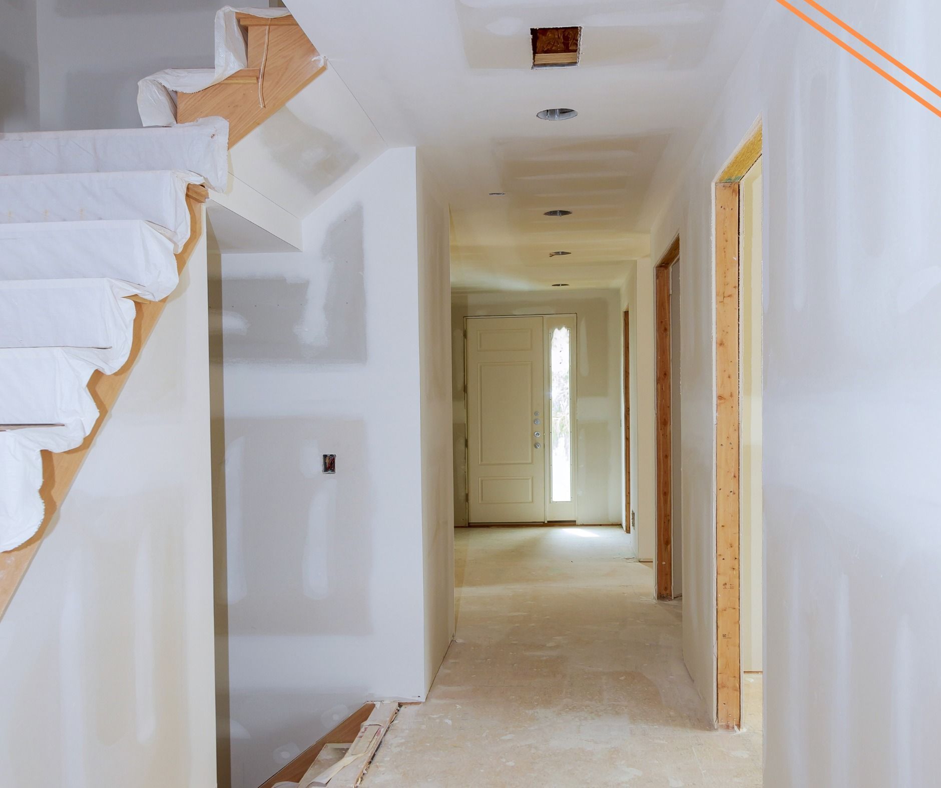 Hallway under construction with a staircase on the left; drywall on walls, open doorways, and bright light at the end.
