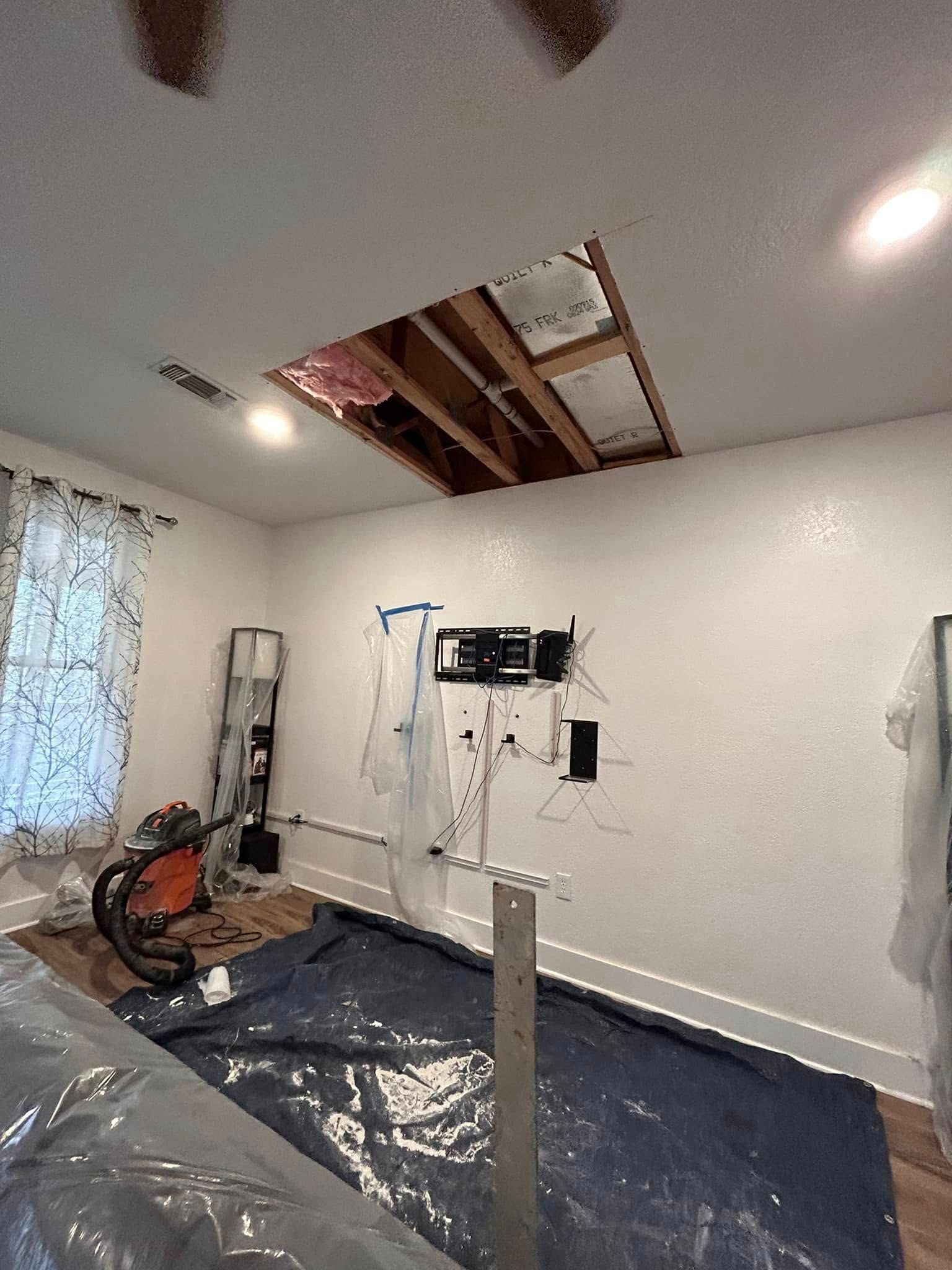 Room under construction; hole in the ceiling reveals beams and insulation. Wires and tools are on the floor.