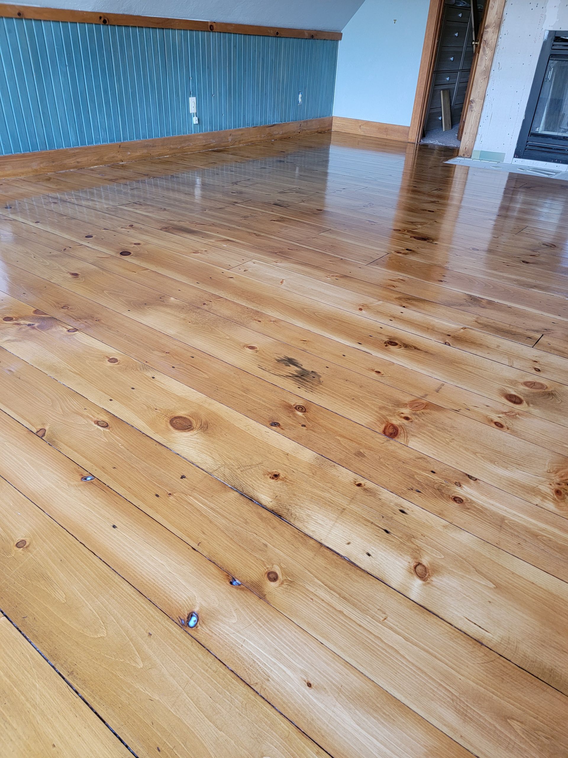 Wooden floorboards in an empty room with blue wallpaper and a window corner