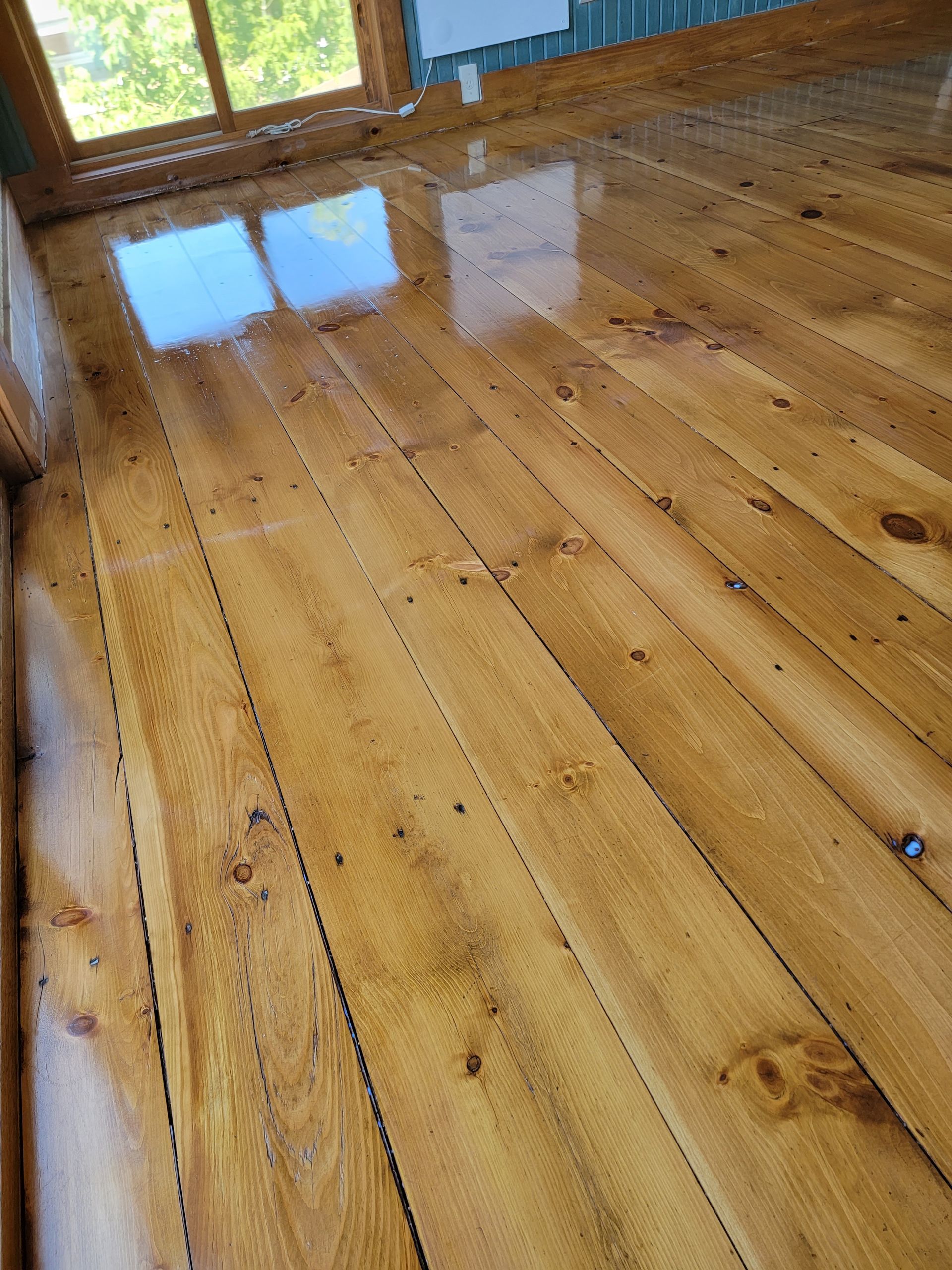 Wooden floorboards in a sunlit room with reflections from a window.