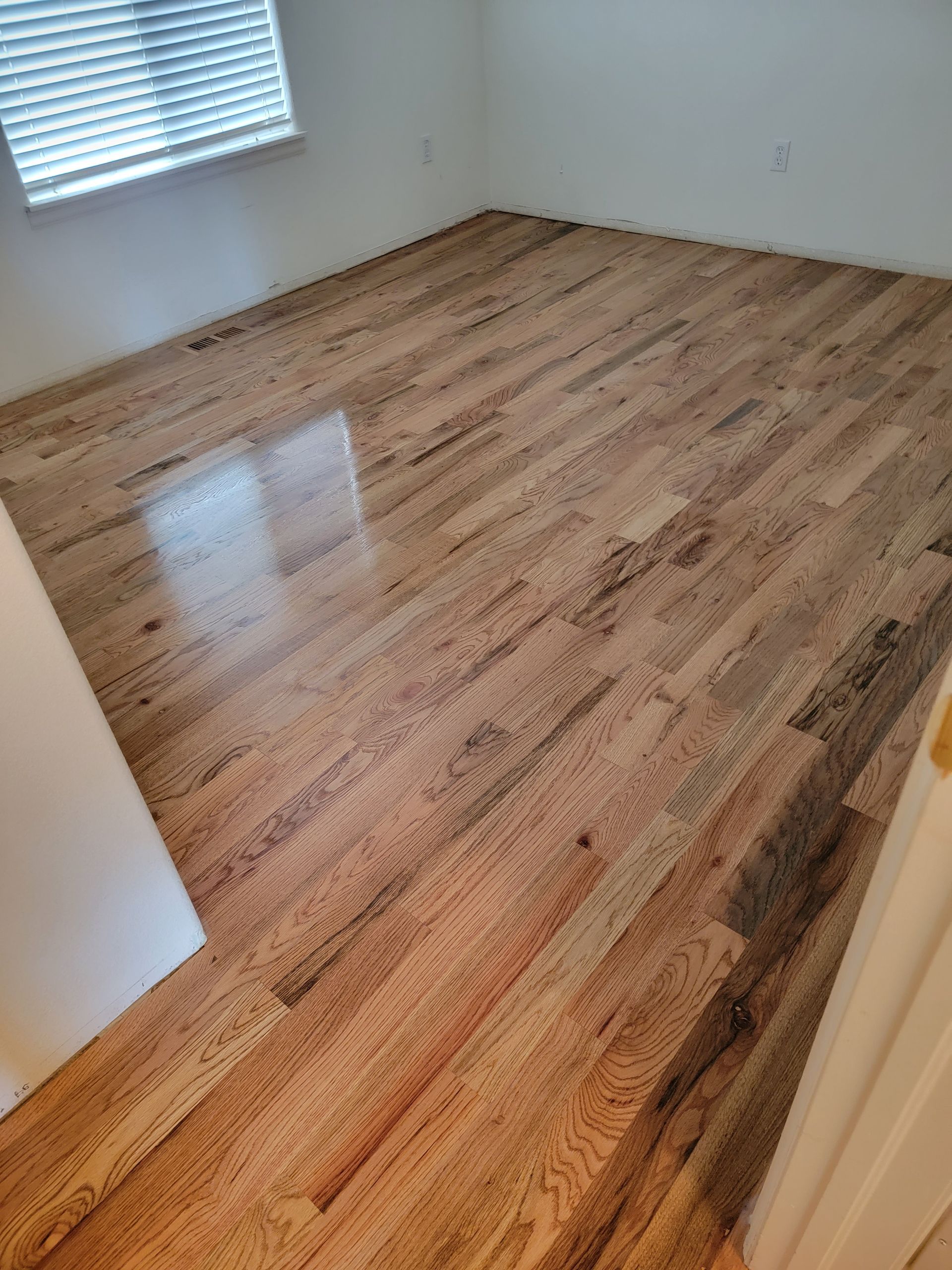 Empty room with refinished hardwood floor and white walls, viewed from the doorway.